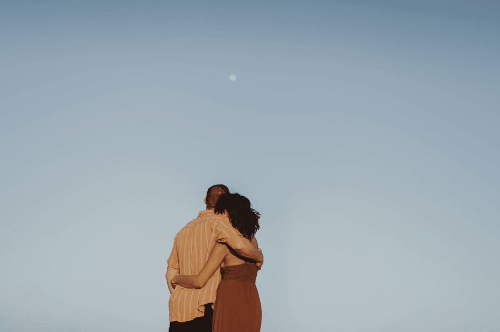 two people hugging looking at the moon in the sky