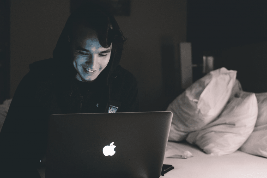 man looking down at his laptop in black hooded sweatshirt, pleased