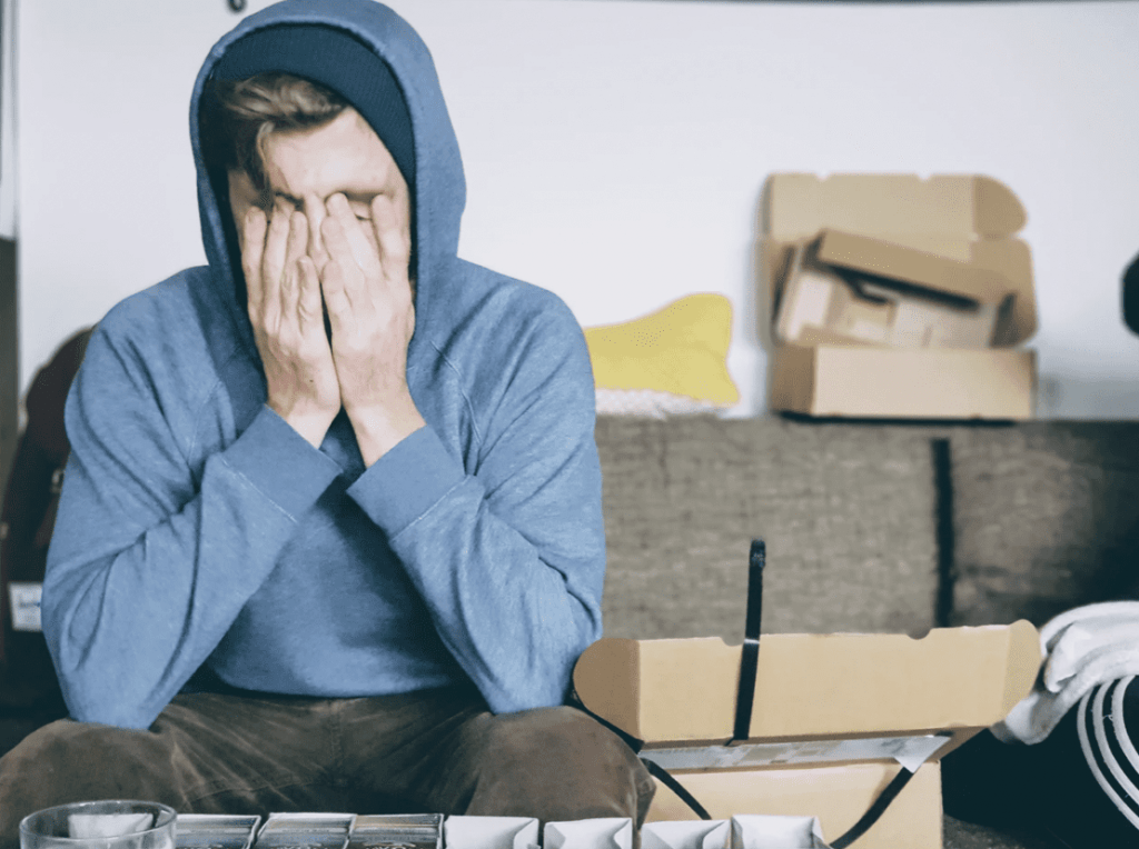 man sat on chair with hood up and head in his hands